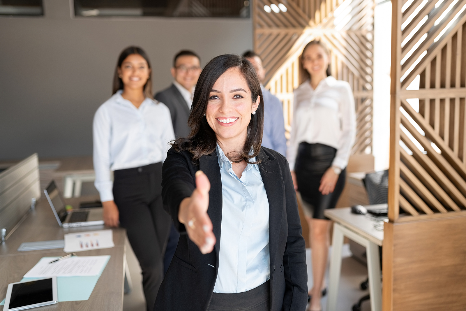Caucasian businesswoman extending her hand for a handshake with colleagues standing in background